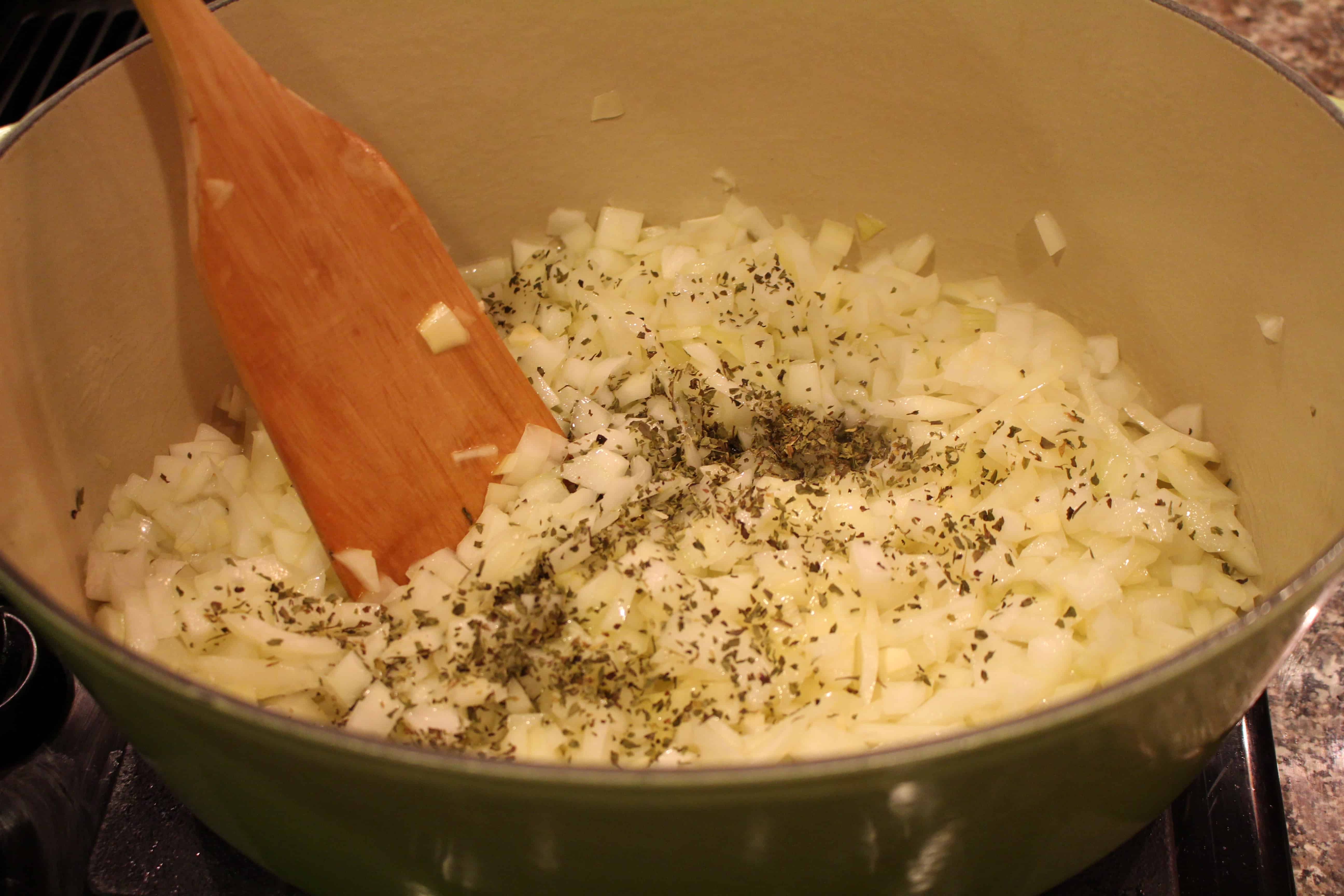 With a wooden spatula, stirring onions, garlic, oregano and salt in a large pot.