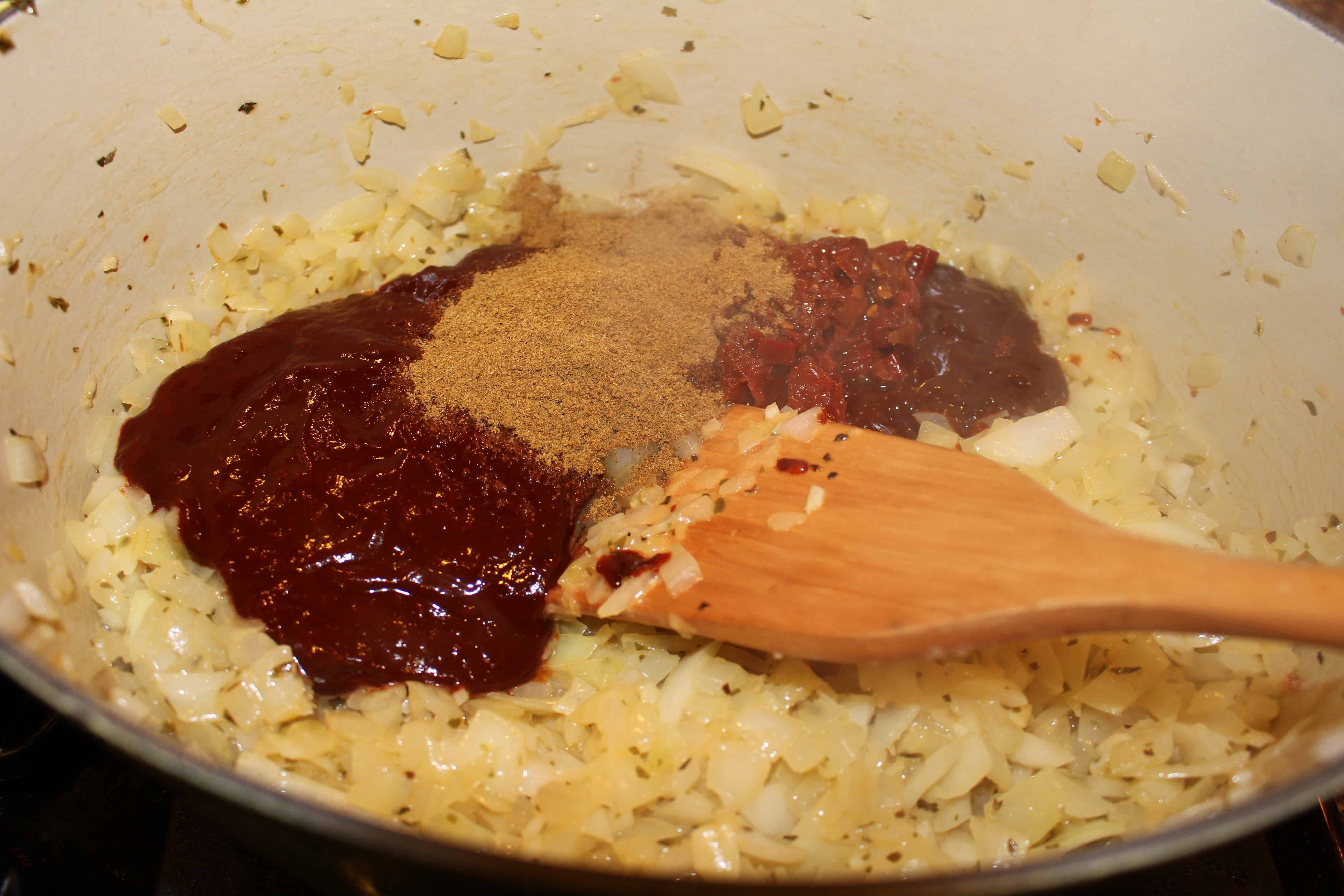 Using a wooden spatula, stirring onions, tomato paste, chili paste and spices in a large pot.