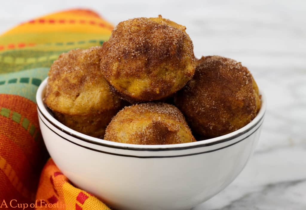 No Fry Pumpkin Donut Holes Rolled in Cinnamon Sugar in a small white bowl with a colorful orange and green napkin next to it.