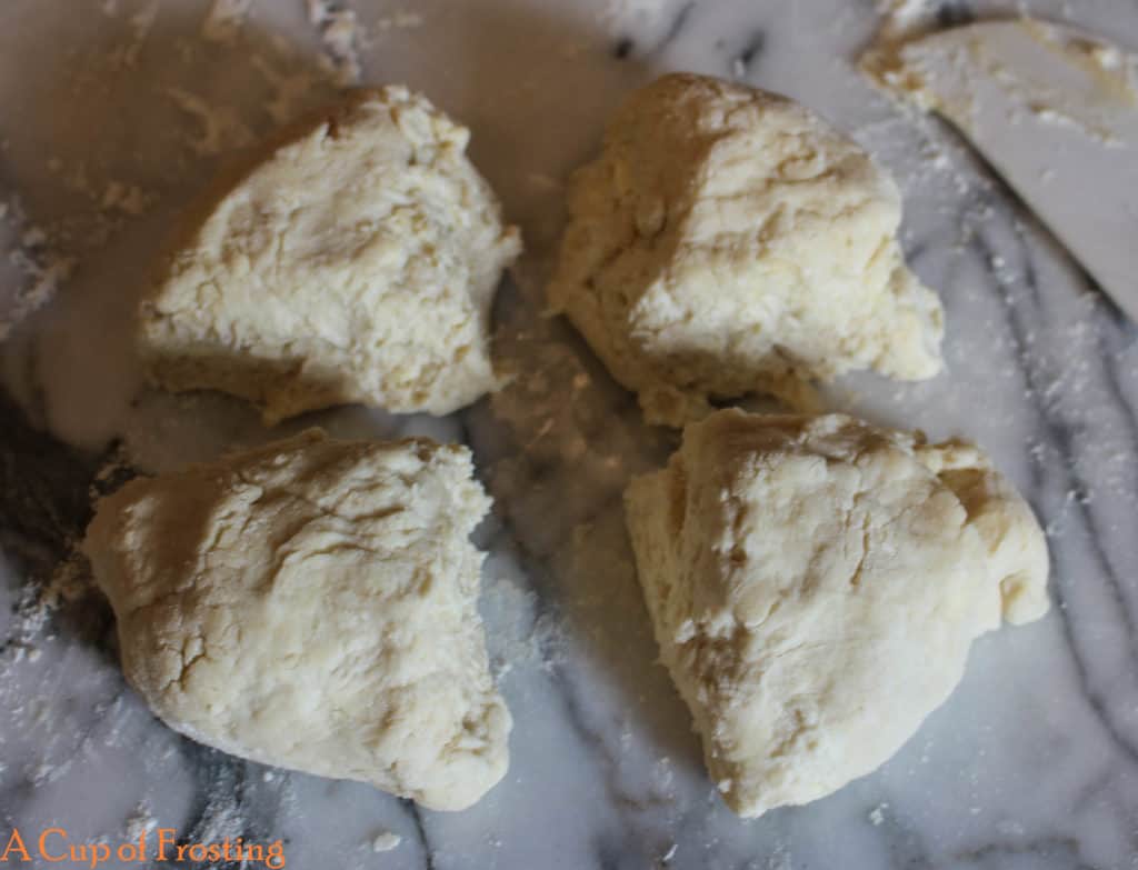 Ball of shortcake dough cut into 4 pieces on a white marble background.