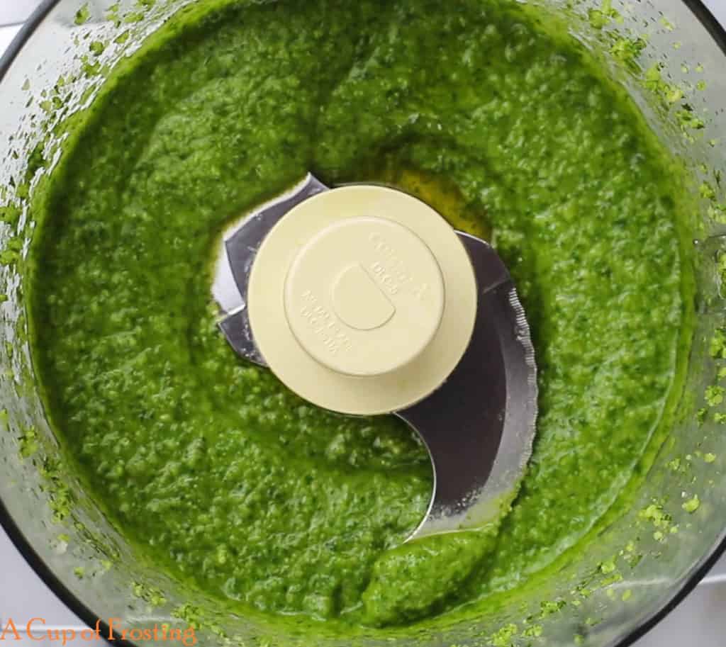 Green pesto that looks smooth in a food processor bowl.
