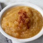 Homemade Applesauce with Cinnamon on top in white bowl with grey napkin on the left side.
