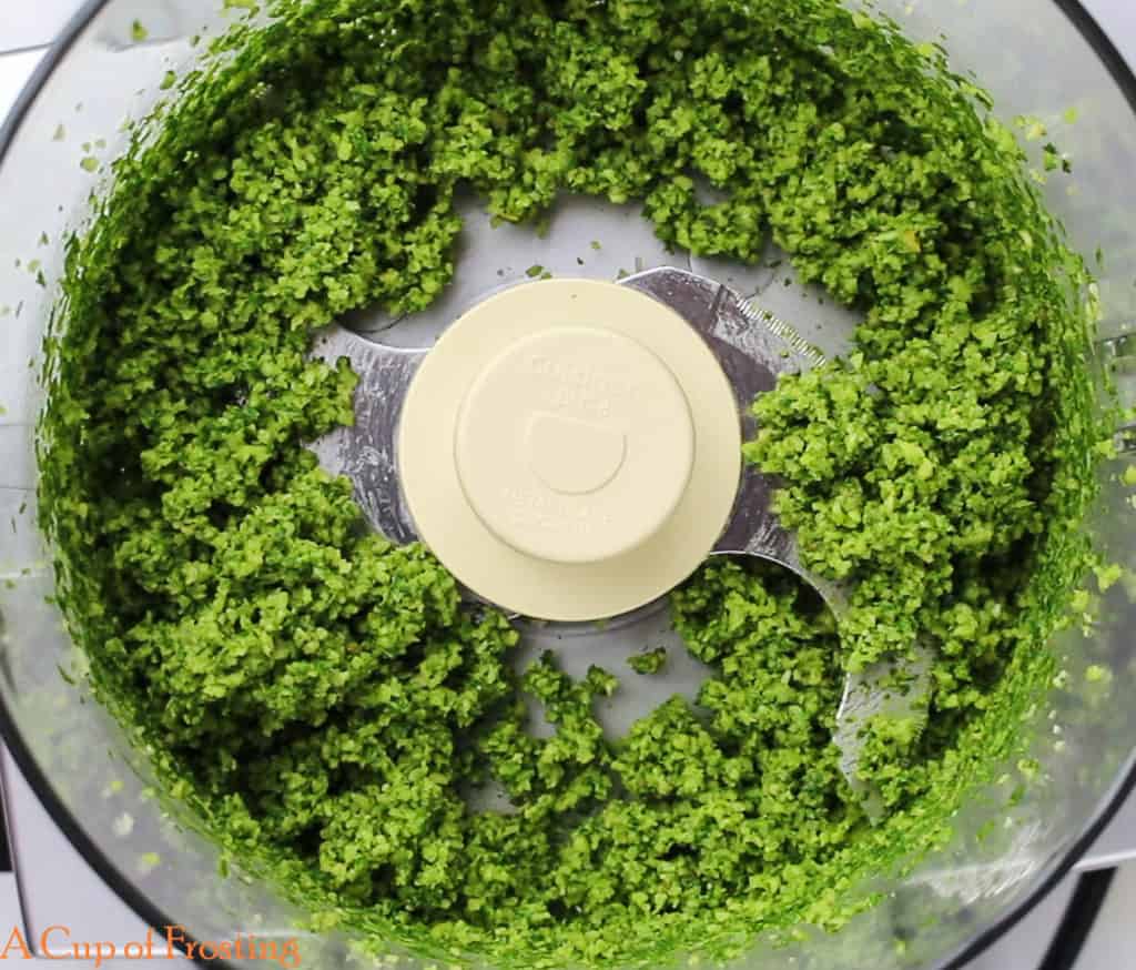 Green pesto that looks chunky in a food processor bowl.