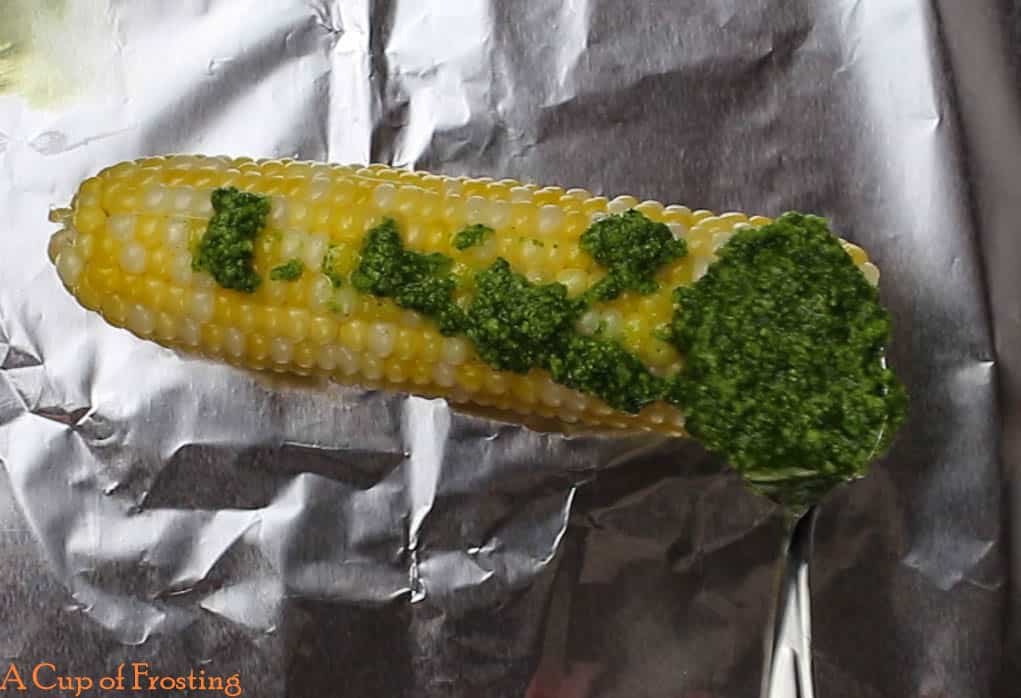 Corn on the cob with green pesto on top lying on a piece of foil.