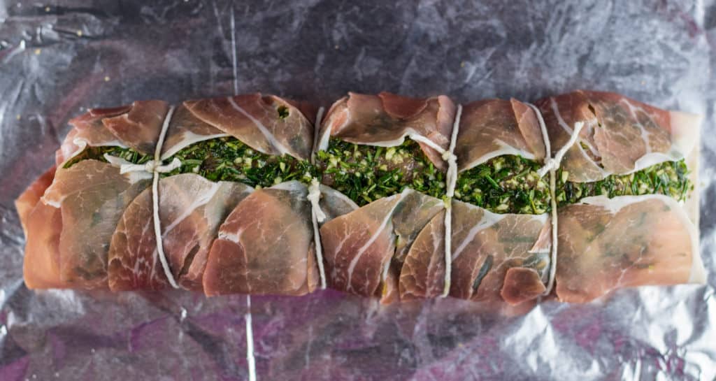 Pork tenderloin covered with the herb mixture on top of 6 pieces of prosciutto all tied together with kitchen twine to form a roll on foil lined baking sheet.