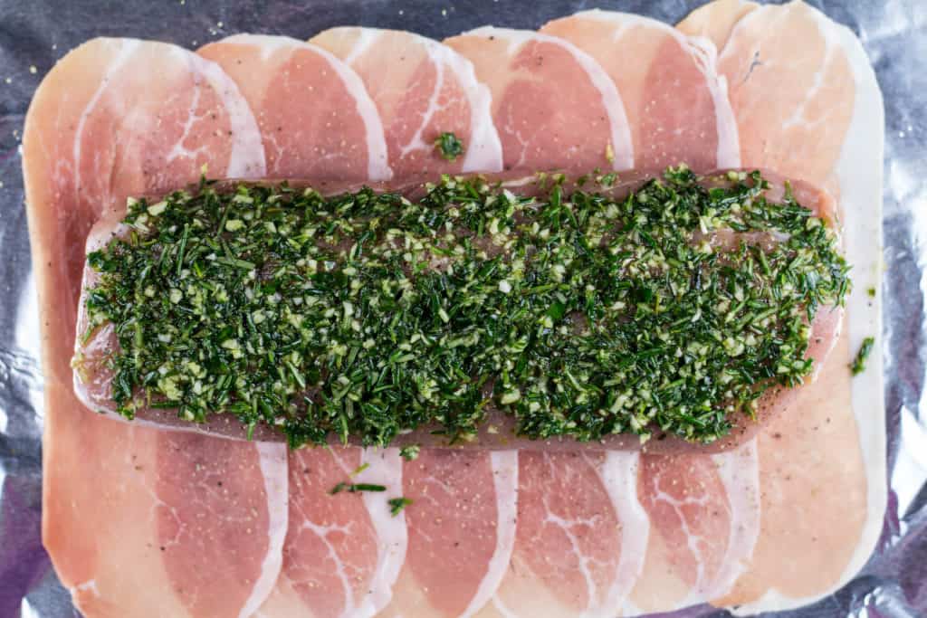 Pork tenderloin covered with the herb mixture on top of 6 pieces of prosciutto laid in a in a rectangle on foil lined baking sheet.