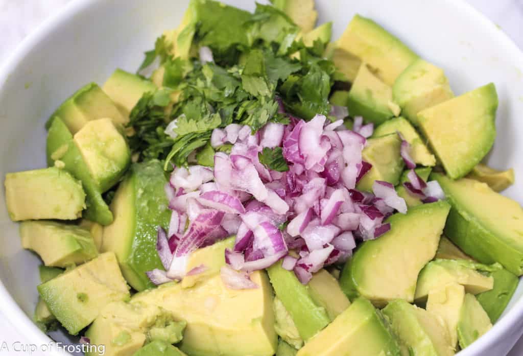 Chunks of avocado, chopped red onion and chopped cilantro in a bowl. 