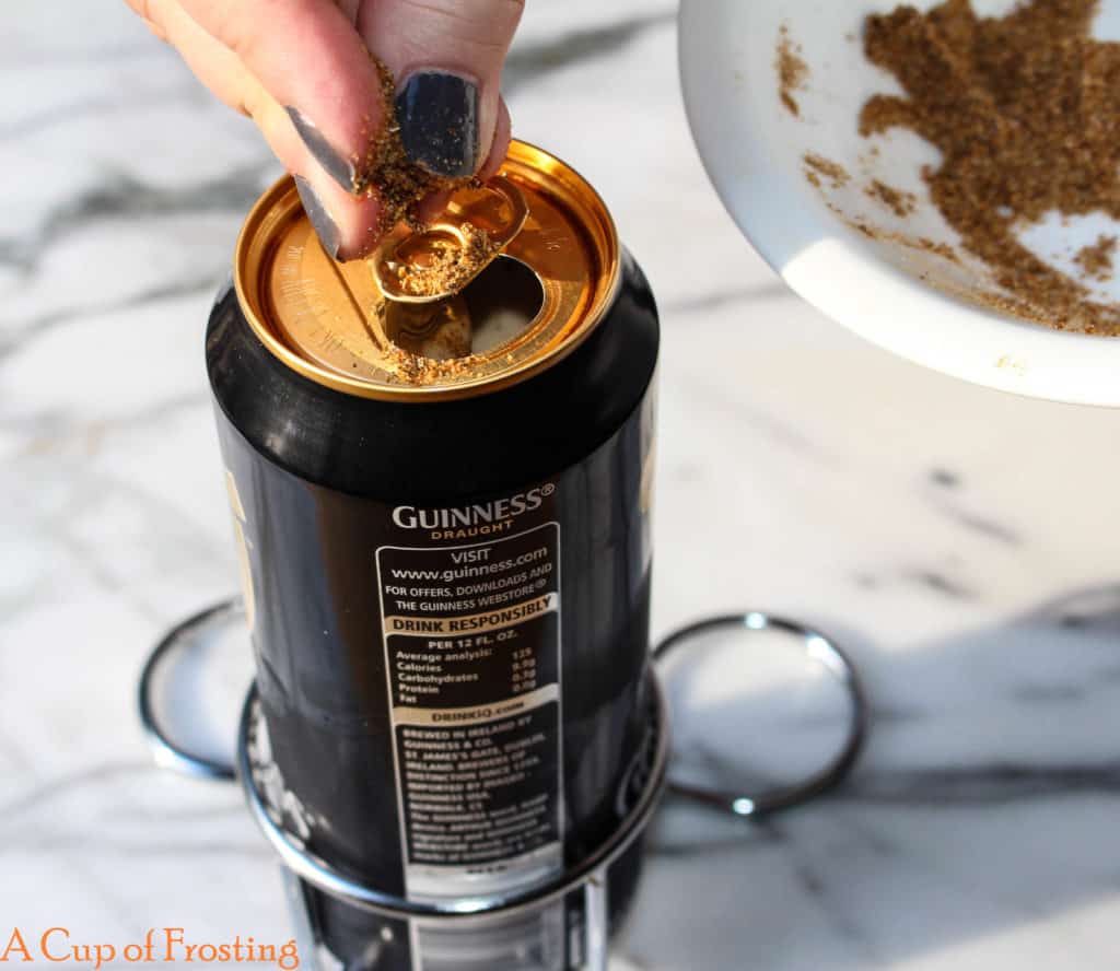 A hand sprinkling spices and herbs into a can of beer in a beer can holder made specifically for BBQing beer can chicken. 