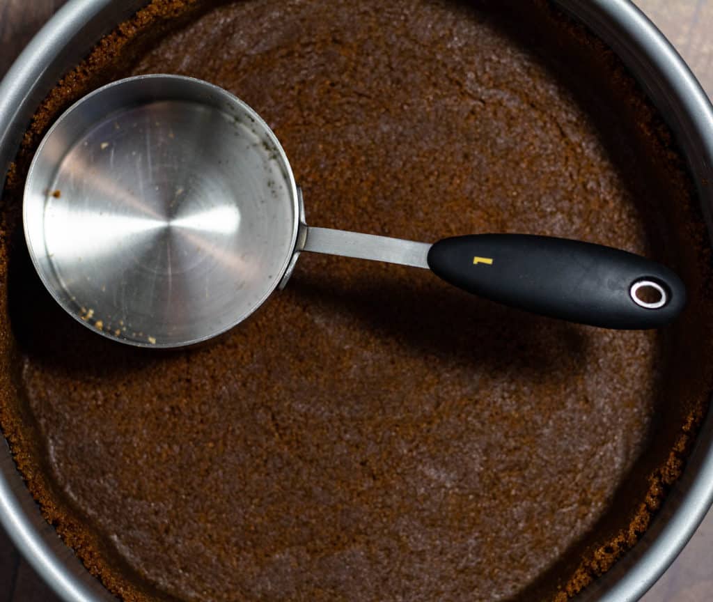 Using the bottom of a measuring cup to spread the cookie crumbs around the spring form pan